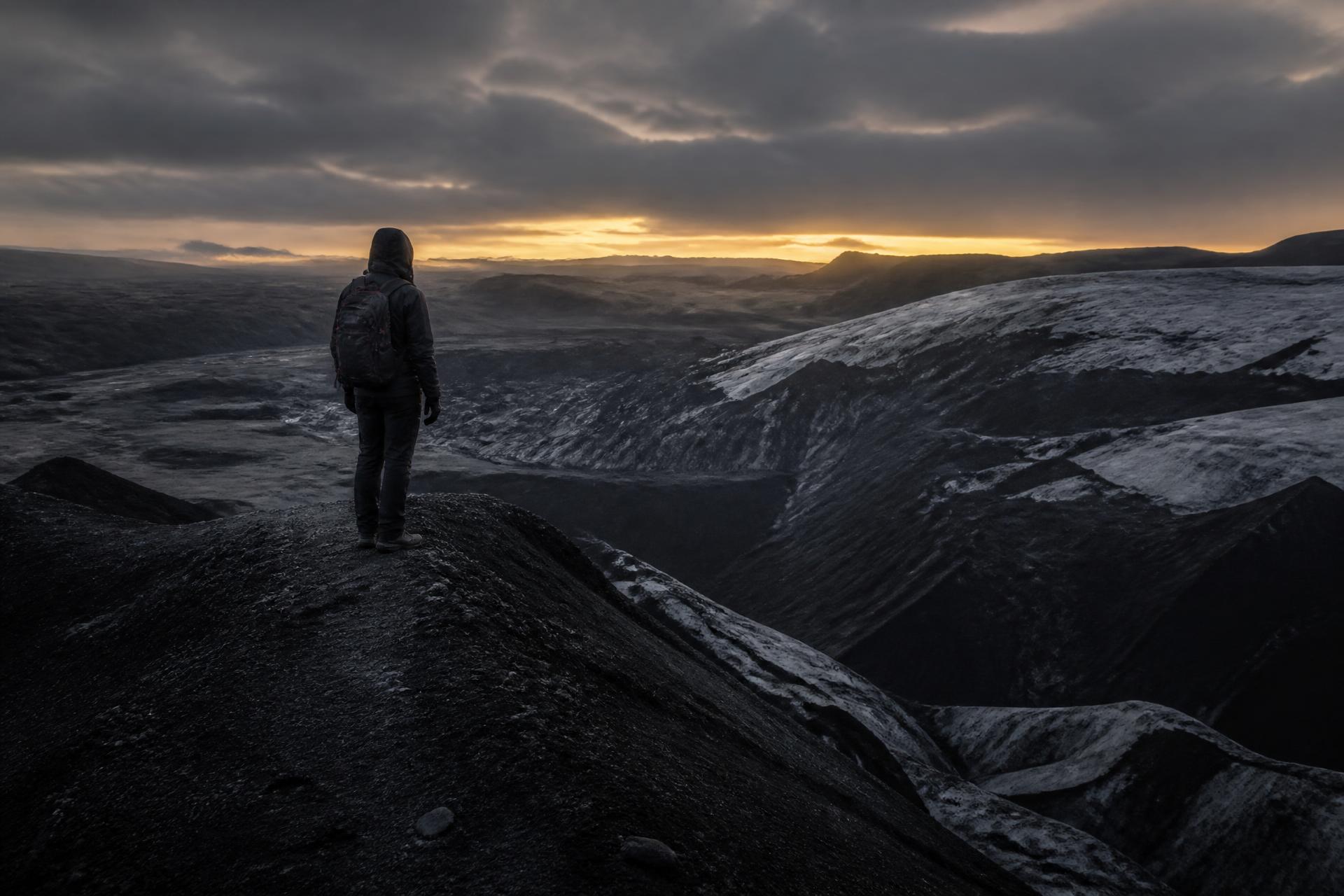 A lone figure on a black glacier ridge at dusk